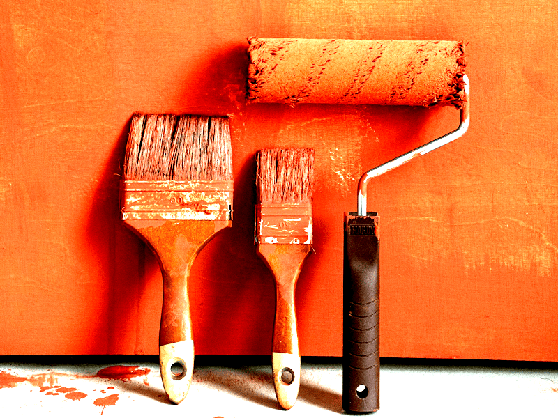 Two paint brushes and a paint roller leaning against a wall - all covered in orange paint; representing DIY SEO.